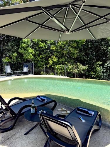 a table and chairs under an umbrella next to a swimming pool at Coolum Beachfront Luxury for Family and Friends in Coolum Beach