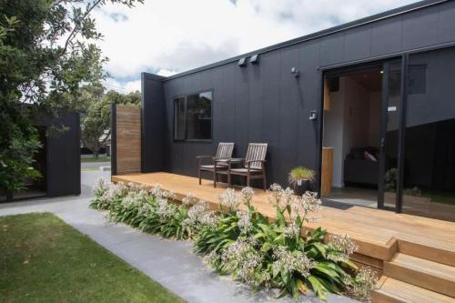 a black house with two chairs on a wooden deck at The Dunes at Fitzroy Beach in New Plymouth