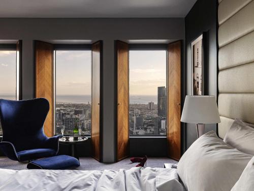 a bedroom with a bed and a chair and windows at Sofitel Melbourne On Collins in Melbourne