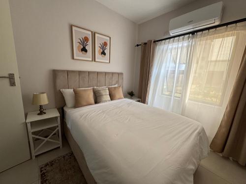 a bedroom with a white bed and a window at The Fig Central Apartments in Gaborone