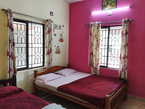 a bedroom with pink walls and two beds with windows at The Homely Stay - Chandransh Homestay in Udupi