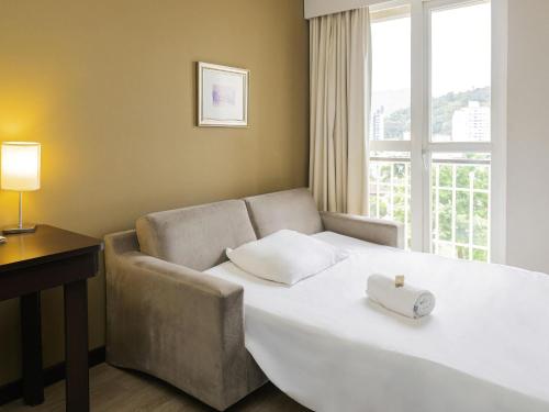 a bedroom with a bed and a couch and a window at Mercure Jaragua do Sul in Jaraguá do Sul