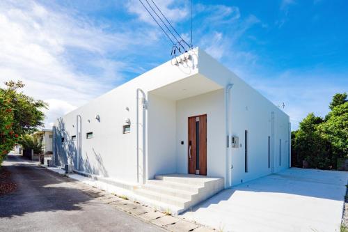 a white building with a wooden door on a street at シャングリラ沖縄 in Motobu
