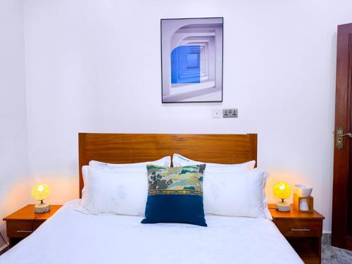 a bedroom with a white bed with two lamps at Maja Apartments Kampala in Kampala