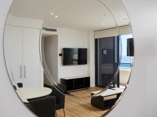 a mirror reflecting a room with a table and a tv at Ruby Apartment Gold Coast in Gold Coast