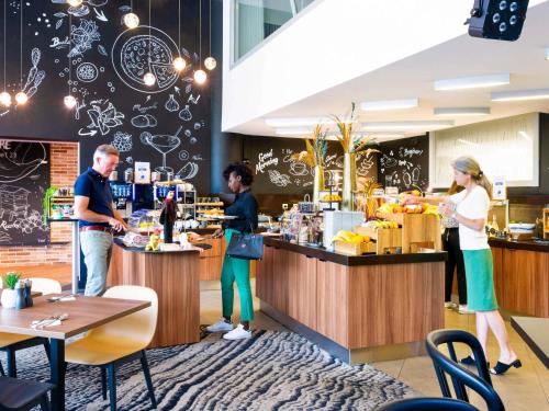 a group of people standing at the counter of a restaurant at Novotel Lyon Centre-Confluence Bord de Saone in Lyon