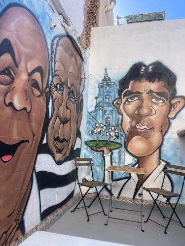 a wall with a mural of two men and chairs at Casa ARANAL in Málaga