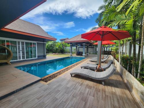 a pool with two chairs and a red umbrella at Khaolak Yama Resort - SHA Plus in Khao Lak