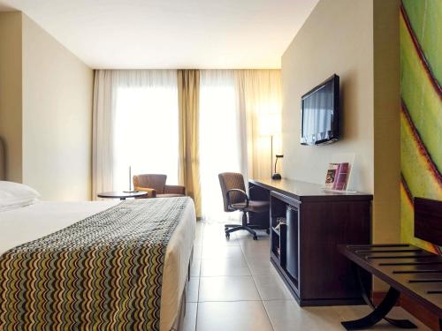 a hotel room with a bed and a flat screen tv at Mercure Salvador Pituba in Salvador