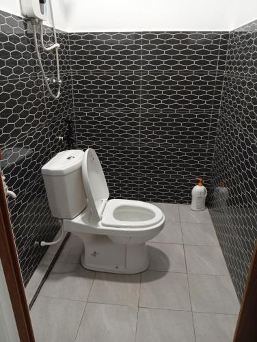 a bathroom with a toilet and a black tiled wall at ibilik Changloon in Changlun
