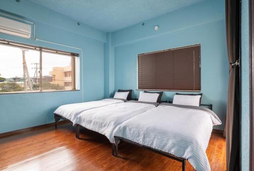 two beds in a blue room with two windows at 一棟貸しハウスまれち in Kumejima