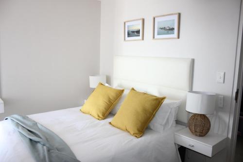 ein weißes Schlafzimmer mit einem Bett mit gelben Kissen in der Unterkunft Luxurious 3-bedroom Bloubergstrand Cape Town beachfront apartment with stunning sea and beach view in Cape Town