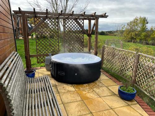 a hot tub sitting on a patio next to a bench at Hedgehog Glamping Pod in Leighton