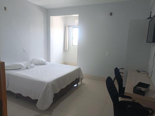 een witte slaapkamer met een bed en een stoel bij Hotel Rio do Ouro in Porangatu