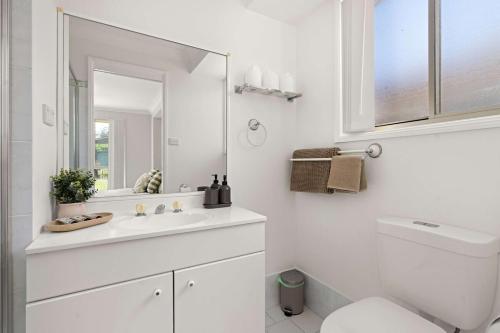 a white bathroom with a sink and a mirror at Bay Breeze Cottage in Callala Bay