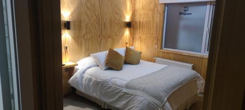 Un dormitorio con una cama con dos almohadas y una ventana. en Departamentos Dragones Puerto Natales, en Puerto Natales