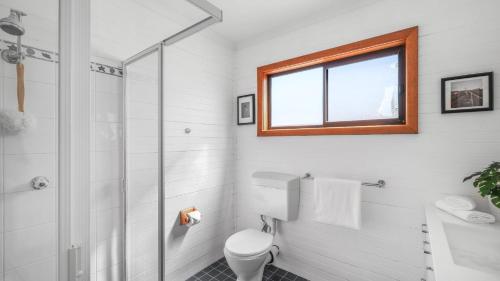 a bathroom with a toilet and a shower and a window at King Stingray in Currarong
