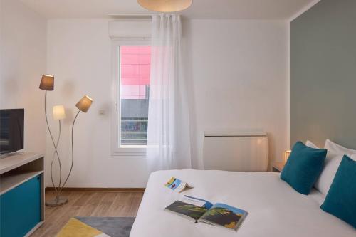 Un dormitorio con una cama blanca con almohadas azules y una ventana en Quality Suites Valenciennes, en Valenciennes