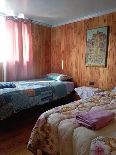 two beds in a room with wooden walls at Casamaiga hostal in Chaitén