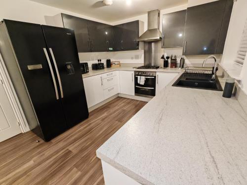 a kitchen with a black refrigerator and white cabinets at Garland Modern 4 Bedroom House with Garden & Parking in Kent