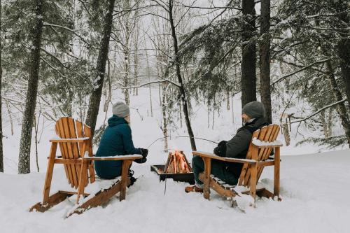 zwei Personen sitzen um ein Feuer im Schnee in der Unterkunft Le 88 Howard - Spa Sauna River & Cute Bridge in Mansonville