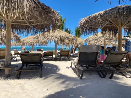a group of chairs and straw umbrellas on a beach at Cocotal 2beds apartament Golf Course Melia Beach PC RD in Punta Cana