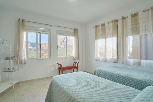 a bedroom with two beds and a chair and windows at La pincelada de Mágina in Bedmar