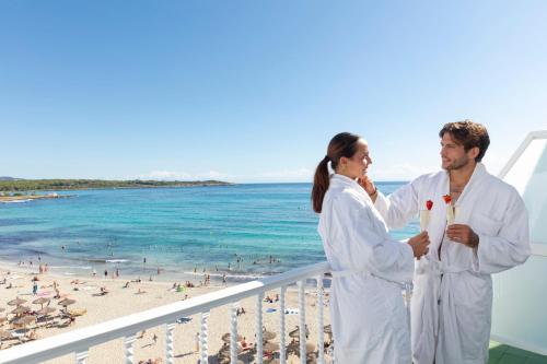 a man and woman standing on a balcony at the beach at Hotel Club S'Illot in S'Illot