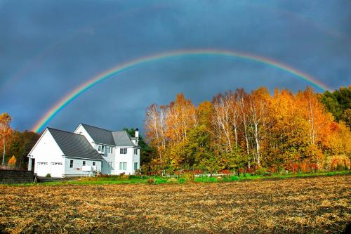 a rainbow over a house in a field at 丘の上白亜の洋館風別荘静かな小さなお宿 3階屋根裏部屋ロフトタイプ 3ベッドルームキッチン洗濯機なし in Asahikawa