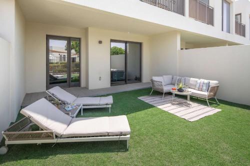a patio with white furniture and green grass at Frank Porter - Parkside 2, Emaar South in Ghantoot