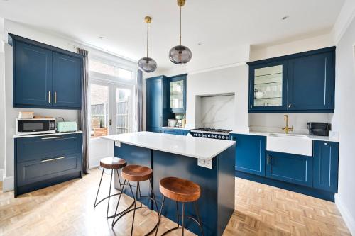 una cocina con armarios azules y taburetes en Chic House With Free Parking and Private Backyard, en Harrow