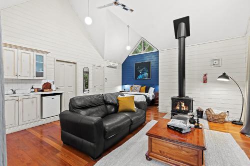 a living room with a black leather couch and a stove at Two Truffles Cottage Accommodation in Yarra Glen