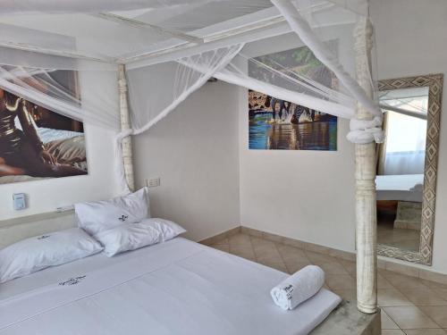 a white bedroom with a bed and a mirror at Nyumba Maua B&B in Watamu