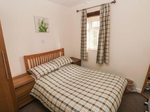 a bedroom with a bed with a checkered blanket and a window at Knap Cottage in Walton East