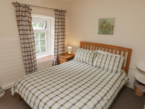 - une chambre avec un lit doté d'une couverture en damier et d'une fenêtre dans l'établissement Stable Cottage, à Walton East
