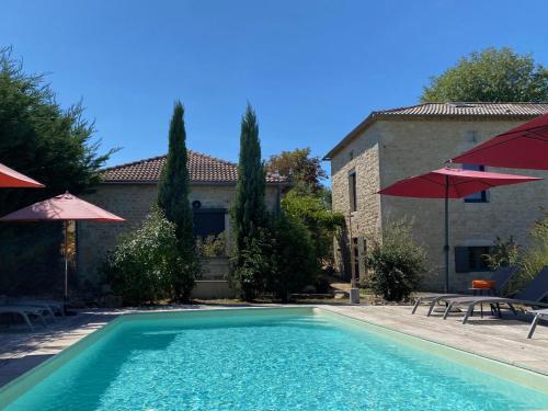 a swimming pool in front of a house with umbrellas at Maison Reces in Floressas