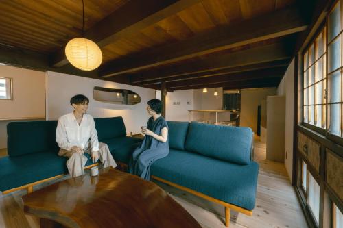two people sitting on blue couches in a living room at 帰々Kiki in Yamatokoriyama