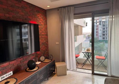 Una sala de estar con televisión y una pared de ladrillos. en Studio Zenata Central Park Près de la plage Vue Piscine, en Aïn Harrouda
