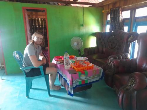 Homestay Komodo Paradise في Pulau Komodo: رجل يجلس على طاولة في غرفة المعيشة