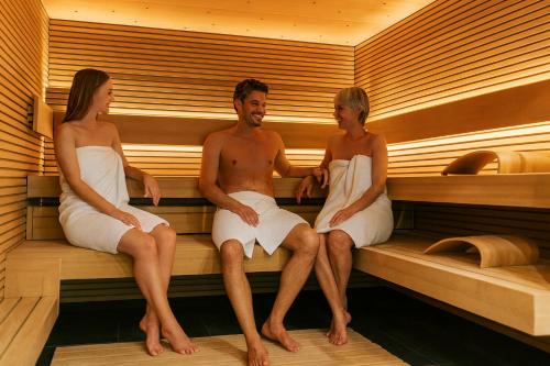 un homme et deux femmes assis dans un sauna dans l'établissement Harmony Deluxe Chalet, Sauna & Fireplace by Belle-Stay, à Reith bei Kitzbühel