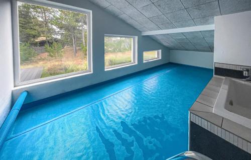 a swimming pool with a blue floor in a room with two windows at Nice Home In Blåvand With Sauna in Blåvand