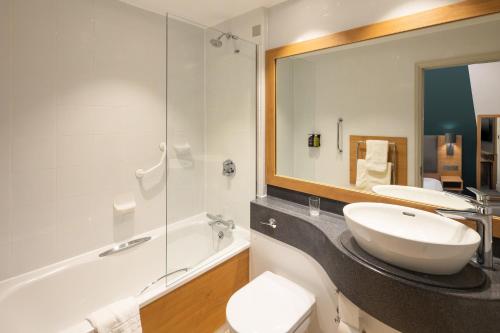 a bathroom with a sink and a tub and a mirror at Holiday Inn Farnborough by IHG in Farnborough