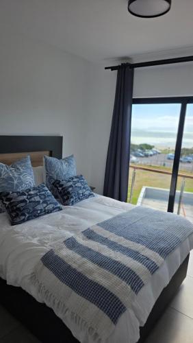 a bed with a blue and white blanket and a window at Modern Sea and Mountain View Apartment - Gordon's Bay in Gordonʼs Bay