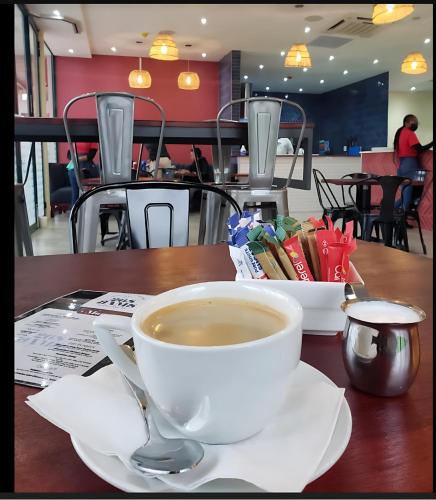 una taza de café sentada en una mesa con una cuchara en Woodland Suites with Airport Shuttle, en Mbabane