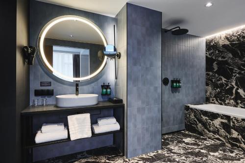a bathroom with a sink and a mirror and a tub at voco Katowice by IHG in Katowice