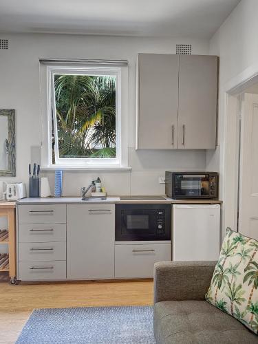 a kitchen with white cabinets and a couch and a window at Cute 1 bedroom with sunny courtyard garden in Sydney