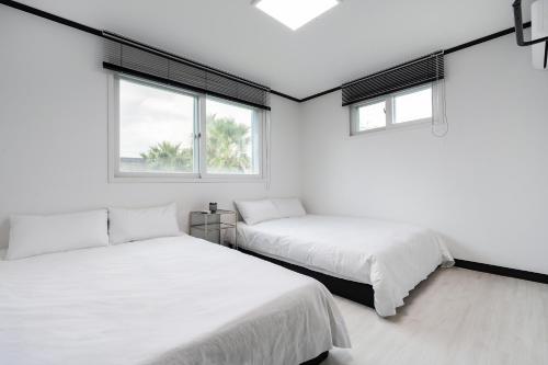 two beds in a white room with two windows at Domostay in Seogwipo