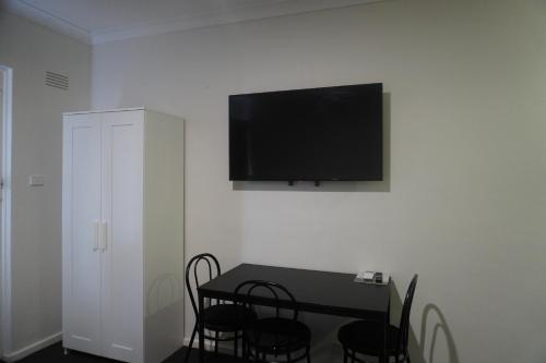 a dining room table with chairs and a television on a wall at Wagga Gardens Motel in Wagga Wagga