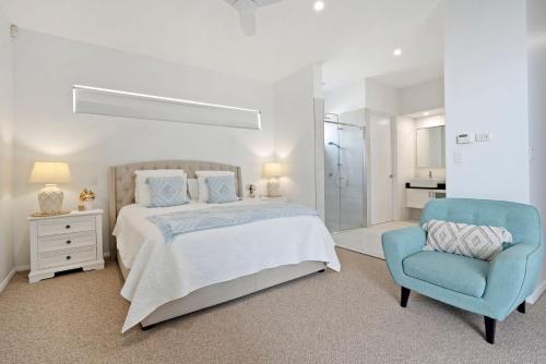 a white bedroom with a bed and a blue chair at Ocean Breeze on Malibu in Kingscliff