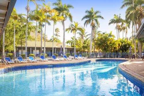 a large swimming pool with chairs and palm trees at Nightcap at Kondari Resort in Hervey Bay